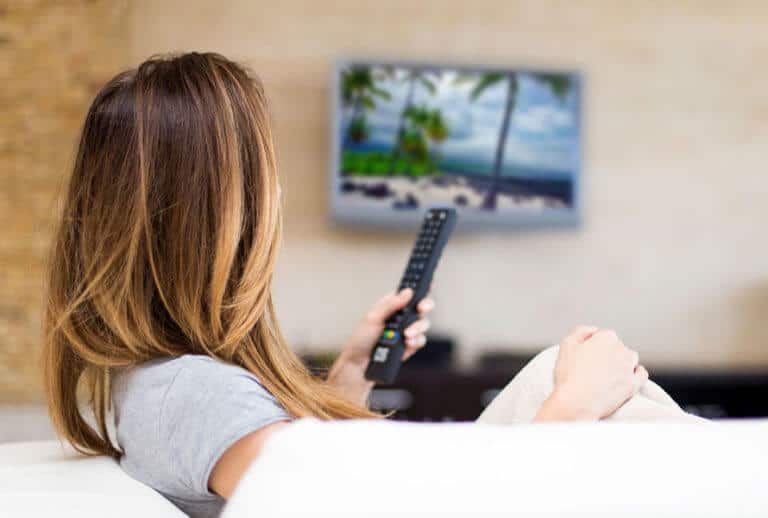 woman sitting on couch holding TV remote